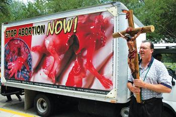 Ric Dugan stands outside the Student Union while holding a cross to protest abortion Wednesday afternoon. Dugan and others later made multiple passes in a van emblazoned with the phrase "STOP ABORTION NOW!" and depicting an aborted fetus.