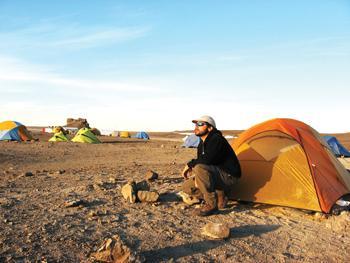 Matthew Reyes, space biologist, crouches by his tent as midnight arrives. Reyes describes the island as "dead and dusty."