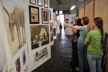 Paintings line the walls in the Old Engineering shops as students browse the art show Friday afternoon.