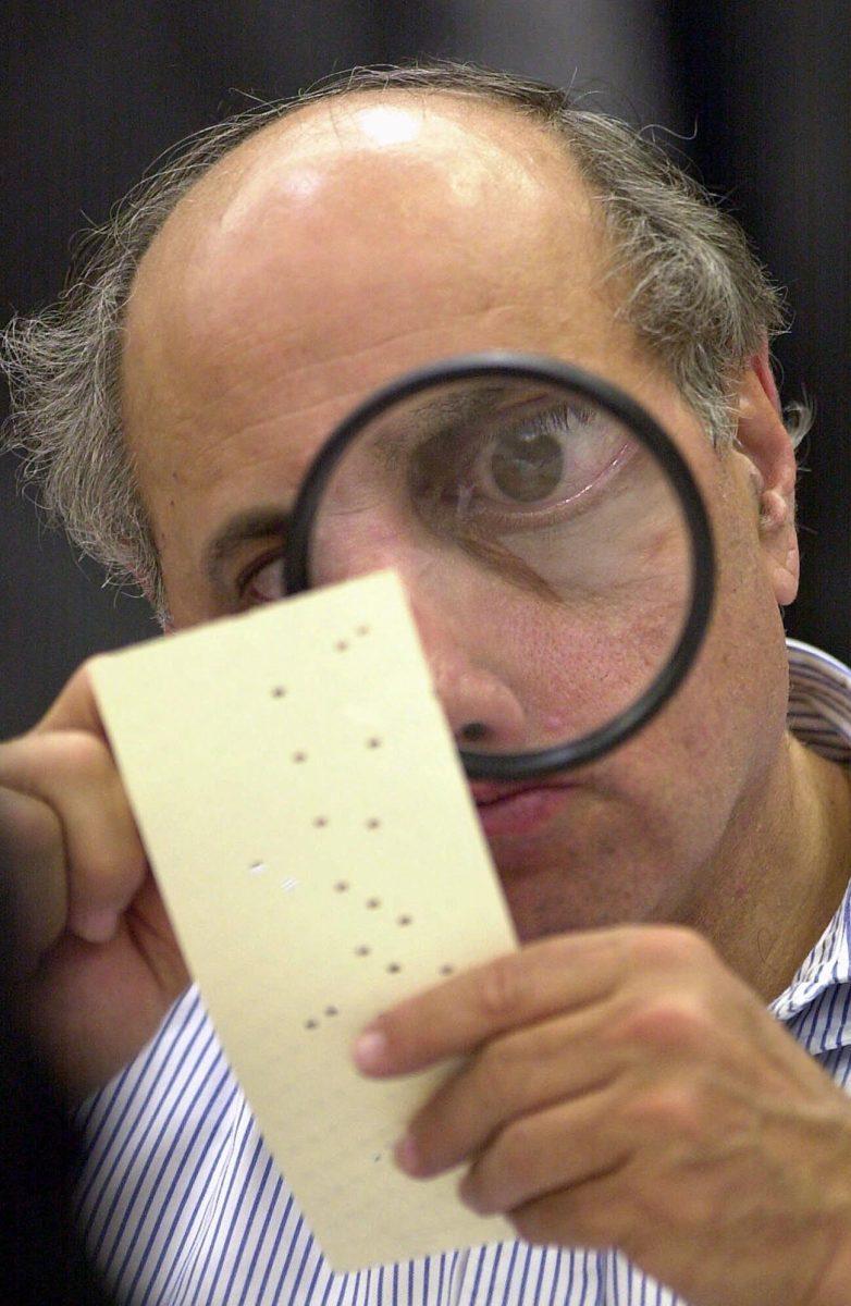 In this Nov. 24, 2000 file photo, Broward County canvassing board member Judge Robert Rosenberg uses a magnifying glass to examine a disputed ballot.