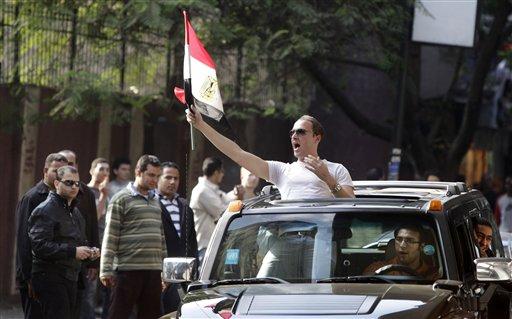 An Egyptian soccer fan standing through the sunroof of a vehicle waves the Egyptian flag and shouts in support as he passes through the area hit by overnight violence between Egyptian soccer fans and riot-police directed towards the Algerian embassy in the Zamalek area of Cairo, Egypt, Friday, Nov. 20, 2009. The Egyptian president's elder son called for a tough stand amid an escalating diplomatic row following the loss to Algeria in a World Cup qualification playoff, as angry soccer fans rioted.