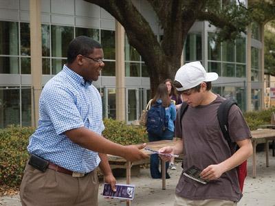 Student Government presidential candidate Theo Williams hands out fliers to a student passing by in Free Spech Alley on Monday.