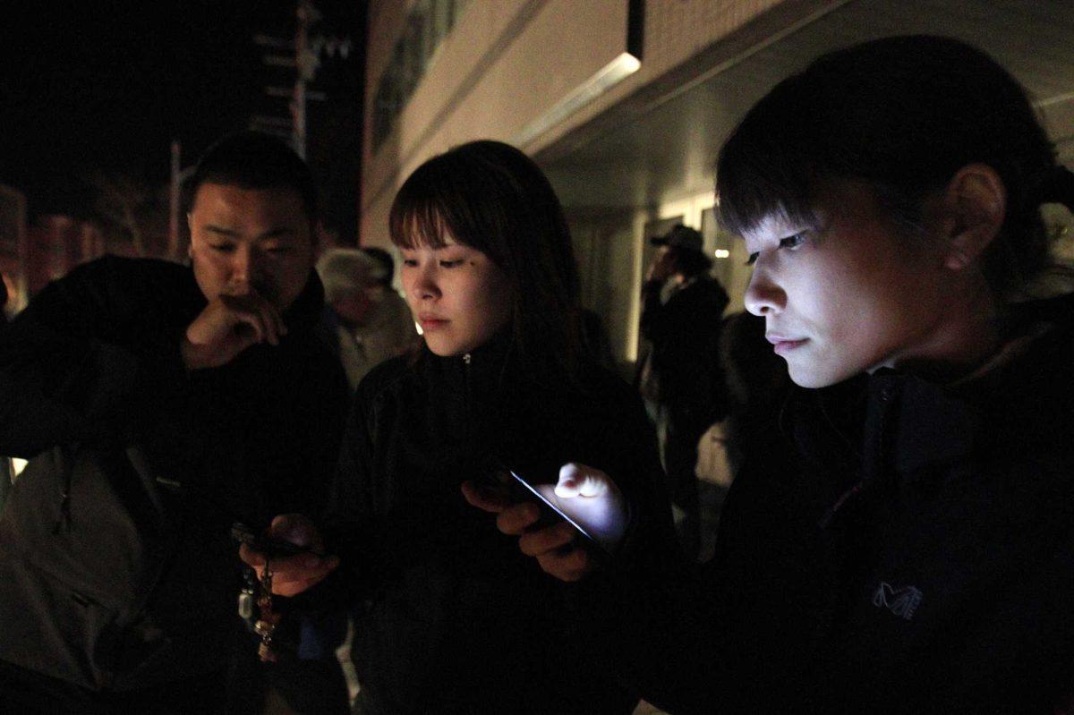 Hotel guests check their phones Thursday for earthquake news after they evacuated the building following an aftershock in Ichinoseki, Iwate Prefecture, Japan.