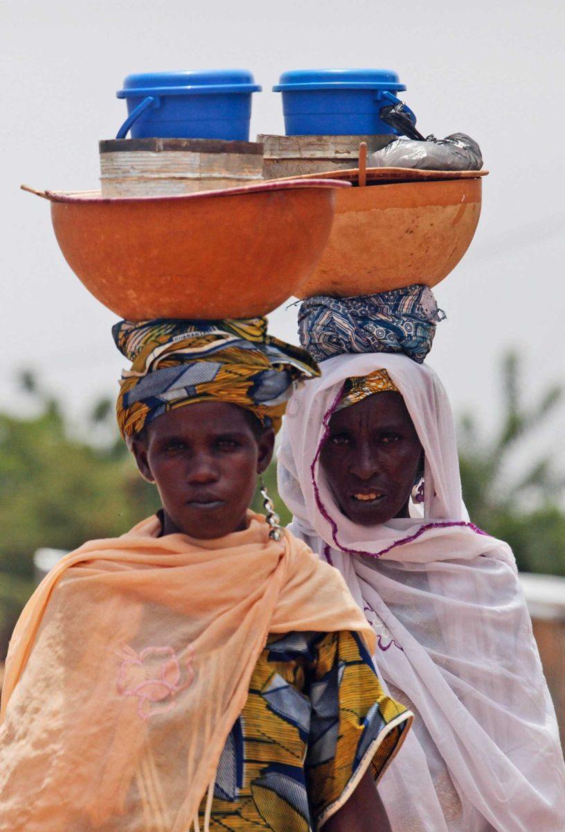 Women selling milk walk past a convoy in Niamey, Niger, Monday, Sept. 12 carrying Moammar Gadhafi&#8217;s son al-Saadi as it crossed into Niger.