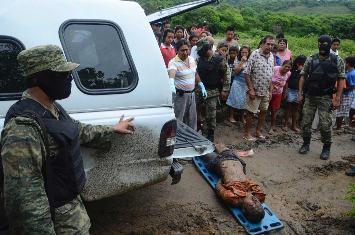 Villagers watch and Mexican army soldiers stand guard Friday as forensic investigators prepare to place a body into a forensic vehicle after the victim was found half buried in the mud in the town of La Venta, entering Acapulco, Mexico.