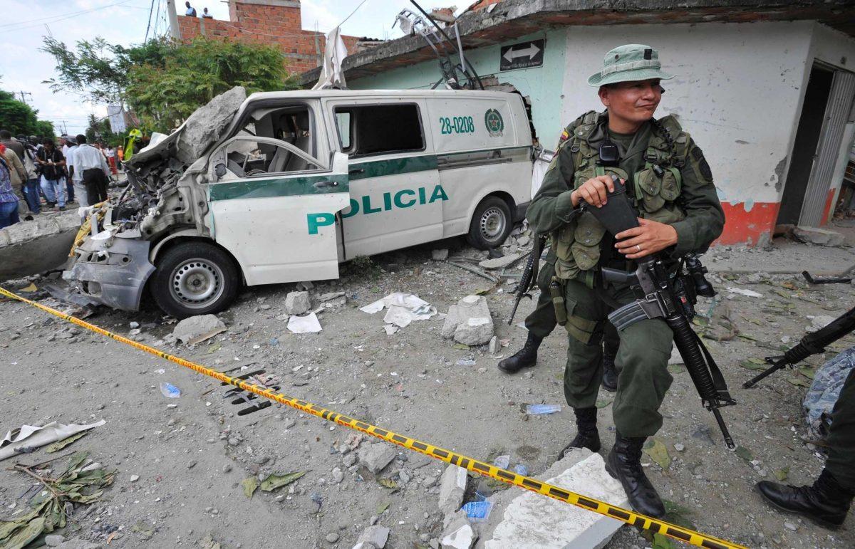 A police officer stands Thursday next to a police vehicle damaged during a homemade mortars attack to the police station in Villa Rica, Colombia.