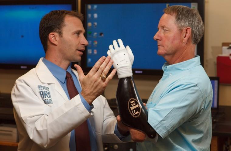 In this Thursday, Sept. 27, 2012 photo provided by Advanced Arm Dynamics, amateur rodeo roper Barry Landry, right, works with his new bionic hand and listens to prosthetist Ron Dodson, in Irving, Texas. Landry doesn&#8217;t know yet if the new hand will let him return to left-handed calf-roping, but says it can already do something the previous model couldn&#8217;t: hold a plate without tipping up. (AP Photo/Advanced Arm Dynamics, Bob Stovall)
 