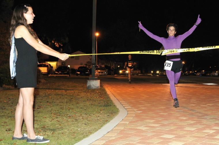 Elementary education senior Kristin Worsham (left) holds a line of caution tape taut as civil engineering freshman Phil DiBenedetto (right) crosses the finish line in first place on Thursday Oct. 25, 2012 at the 2012 Greg Gibbens Ghost Chase 3K Fun Run held at the University Student Recreational Center. The event is held annually to commemorate the life and work of the late Greg Gibbens, a former UREC employee. Participants are encouraged to wear festive costumes and are invited to enjoy refreshments following the race.
 