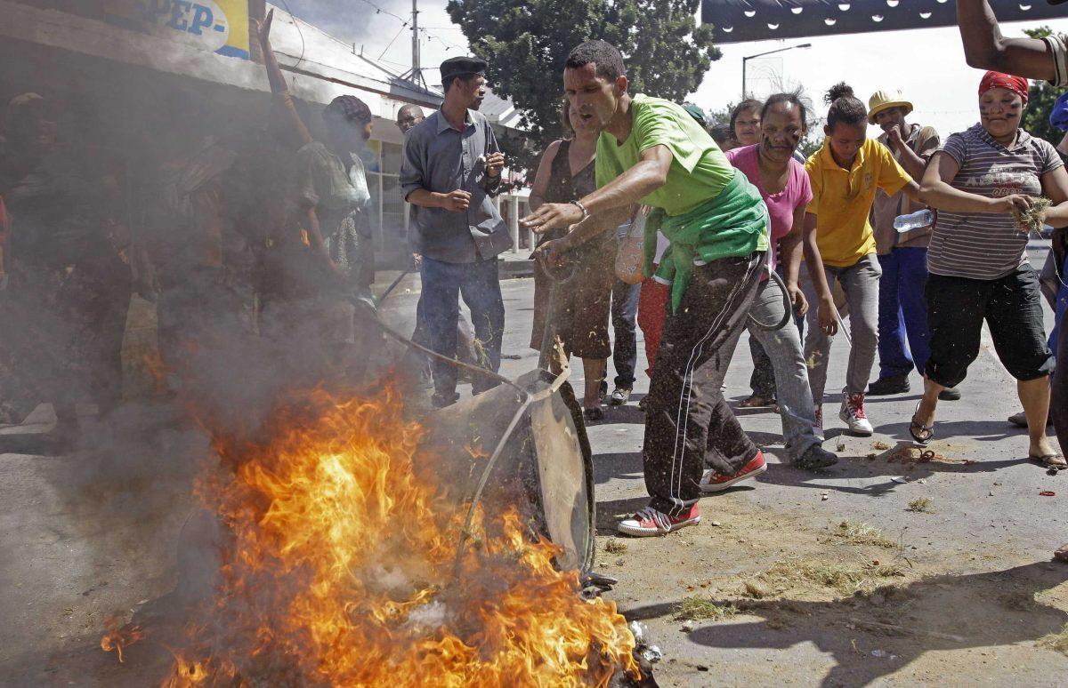 A protesting farm worker puts grass on a fire as he and others protest in the town of Swellendam, South Africa, Thursday, Nov. 15, 2012. Farm workers angered over their minimum daily wages launched a second day of violent protests in the nation's Western Cape, setting fires and marching through the countryside. (AP Photo/Schalk van Zuydam)