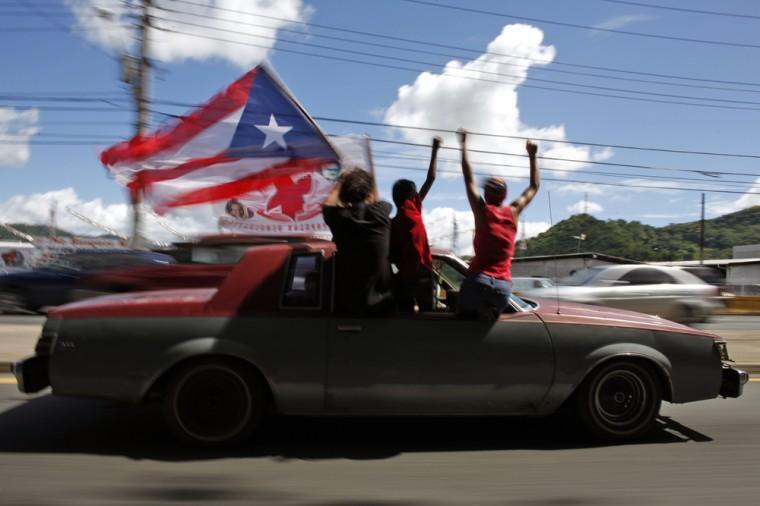 People ride atop a vehicle waving a Puerto Rican flag during elections in San Juan, Puerto Rico, Tuesday, Nov. 6, 2012. Puerto Ricans are electing a governor as the U.S. island territory does not get a vote in the U.S. presidential election. But they are also casting ballots in a referendum that asks voters if they want to change the relationship to the United States. A second question gives voters three alternatives: become the 51st U.S. state, independence, or sovereign free association, a designation that would give more autonomy. (AP Photo/Ricardo Arduengo)
 