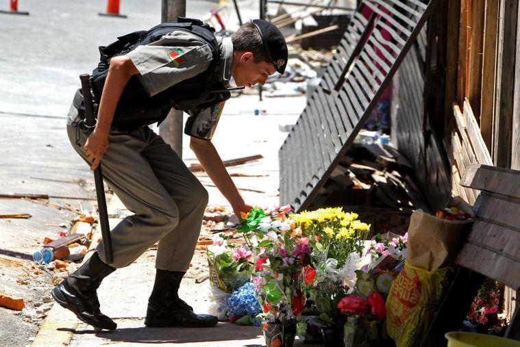 A police officer places flowers outside the Kiss nightclub that were brought by mourners in memory of those who died due to a fire at the club in Santa Maria, Brazil, Monday, Jan. 28, 2013. A fast-moving fire roared through the crowded, windowless Kiss nightclub in this southern Brazilian city early Sunday, killing more than 230 people. Many of the victims were under 20 years old, including some minors. (AP Photo/Nabor Goulart)
 