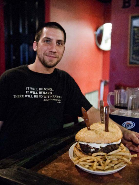 Nick Clough, the cook who made this burger, stands with his creation by the bar in the Londoner Wednesday, Jan. 23, 2013. The forty-ounce burger is on the house for patrons who are able to finish it and its side of fries; if they are unable to, it is $30.00.
 