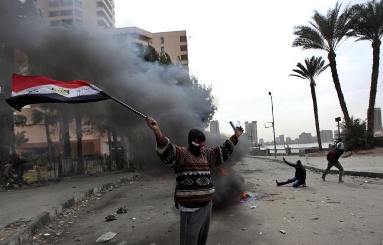 A protester part of the Black Bloc, holds the Egyptian national flag during clashes with riot police near Tahrir Square, Cairo, Egypt, Monday, Jan. 28, 2013. An unpredictable new element has entered Egypt&#8217;s wave of political unrest, a mysterious group of black-masked young men calling themselves the Black Bloc. They present themselves as the defenders of protesters against the rule of President Mohammed Morsi, but Islamists have used them to depict the opposition as a violent force wrecking the nation. (AP Photo/Khalil Hamra)
 