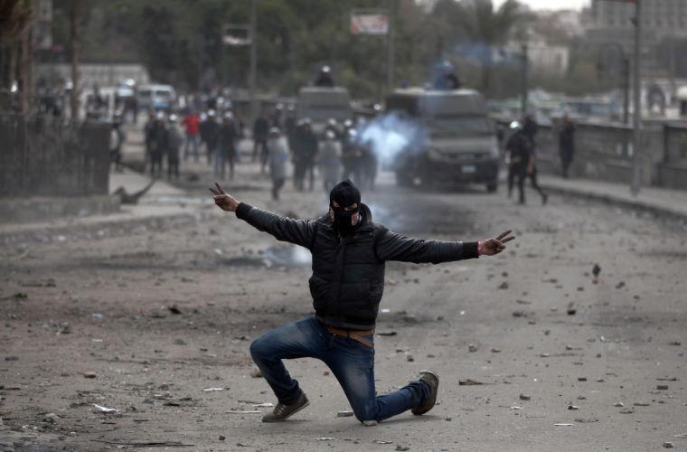 A masked Egyptian protester part of the Black Bloc, flashes the victory sign during clashes with riot police, background, near Tahrir Square, Cairo, Egypt, Monday, Jan. 28, 2013. An unpredictable new element has entered Egypt&#8217;s wave of political unrest, a mysterious group of black-masked young men calling themselves the Black Bloc. They present themselves as the defenders of protesters against the rule of President Mohammed Morsi, but Islamists have used them to depict the opposition as a violent force wrecking the nation. (AP Photo/Khalil Hamra)
 