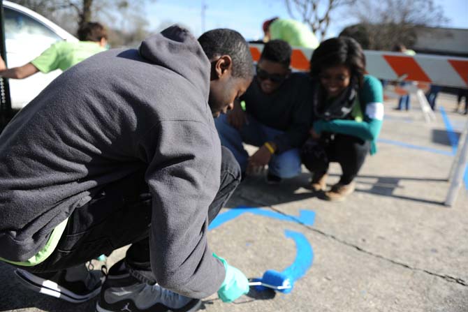 Computer engineering junior John Lewis (left) applies paint to a handicapped parking spot outside of McKinley High School as fellow volunteers look on with enthusiasm Monday Jan. 21, 2013 for the LSU Office of Multicultural Affairs MLK Day of Service 2013.
 