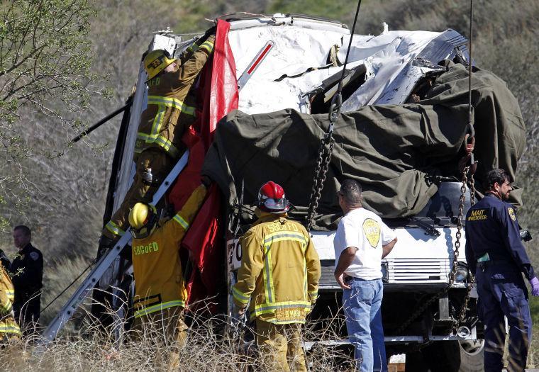 San Bernardino County firefighters hang a drape over the smashed front of a tour bus where at least eight people were killed and 38 people were injured after it collided with tow other vehicles just north of Yucaipa, Calif., Sunday, Feb. 3, 2013. The bus was carying a group from Tijuana, Mexico. (AP Photo/Reed Saxon)
 