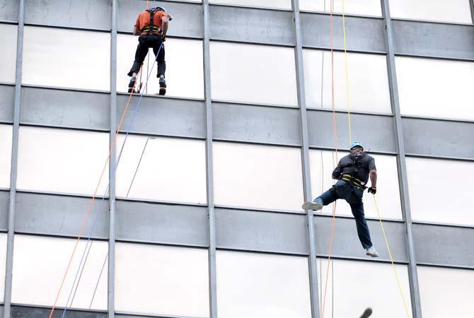 LSU coach Les Miles (right) swings away from the face of the Capitol One building Thursday, May 30, 2013 during his rappel down the 24 story structure in downtown Baton Rouge. Miles' descent is in effort to raise awareness for Louisiana children available for adoption.
 