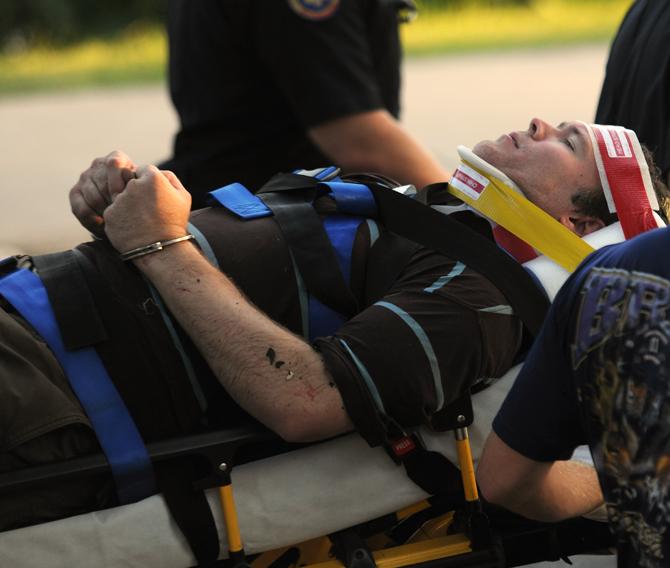 A man is carried away in handcuffs Tuesday, Aug. 27, 2013 after his car flipped into University Lake near the Kappa Alpha Theta sorority house.