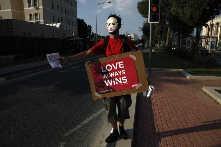 A demonstrator covers his face with a mask representing the Russian President Vladimir Putin , as holds a placard during a demonstration outside the Russian embassy in the capital Nicosia, Tuesday, Sept. 3, 2013. About a dozen gay rights supporters carried placards and chanted slogans outside the Russian embassy to protest Moscow&#8217;s policies on homosexuality. (AP Photo/Petros Karadjias)