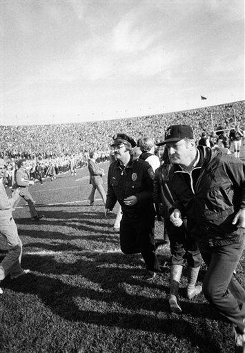 Michigan coach Bo Schembachler makes haste for the locker room accompanied by a policeman, after the University of Minnesota had handed his team their first defeat, 16-0 in Minneapolis, Minnesota, Oct. 22, 1977. (AP Photo)