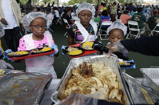 Ashley Logan, 9, left, and Clairvanie Munnings, 9, center, get plates loaded with turkey before serving them to residents during the annual Thanksgiving luncheon, Tuesday, Nov. 26, 2013, in West Park, Fla. Bags of fresh produce, and prepared Thanksgiving meals were also handed out. (AP Photo/Lynne Sladky)