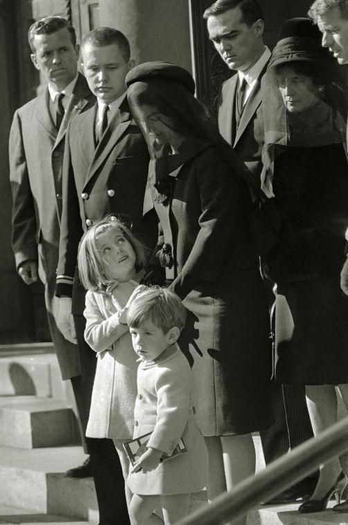 FILE - In this Monday, Nov. 25, 1963 file photo, Caroline Kennedy, 5, looks to her mother, Jacqueline Kennedy, as she clutches her hand, accompanied by John F. Kennedy, Jr., 3, while leaving St. Matthew's Cathedral after the funeral Mass for President John F. Kennedy in Washington. It is his third birthday; his sister will turn 6 two days later. Behind them are Robert P. Fitzgerald, first cousin of the president, Rose Kennedy, mother of the president, and Robert F. Kennedy, his brother, far right. Men at left are unidentified. (AP Photo/William C. Allen, File)