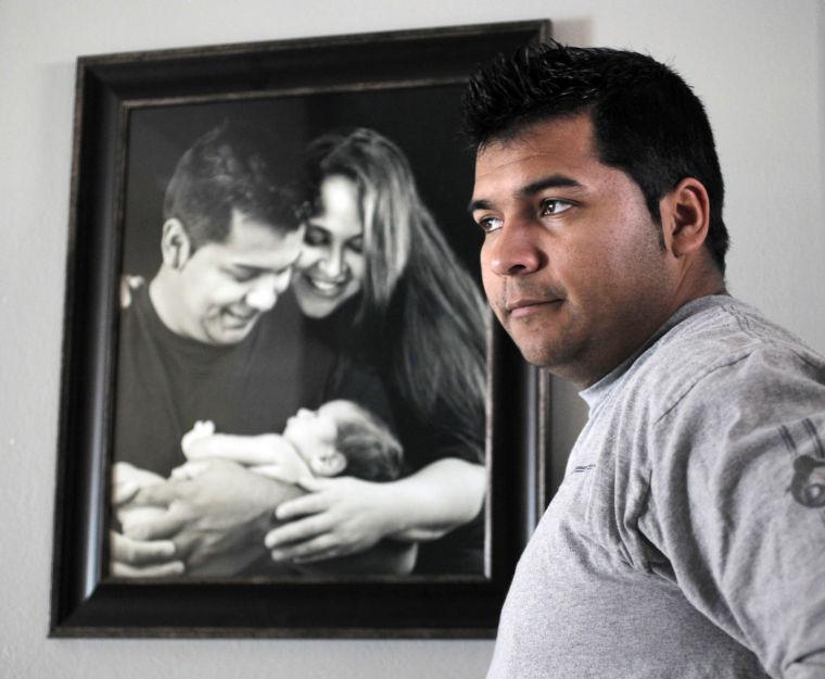 In this Friday, Jan. 3, 2014 photo, Erick Munoz stands with an undated copy of a photograph of himself, left, with wife Marlise and their son Mateo in Haltom City, Texas. Munoz filed a lawsuit in state district court in Fort Worth, Texas, where his wife has been on life support since he found her unconscious in their home on Nov. 26, 2013. She was 14 weeks pregnant at the time. (AP Photo/The Fort Worth Star-Telegram, Ron T. Ennis)