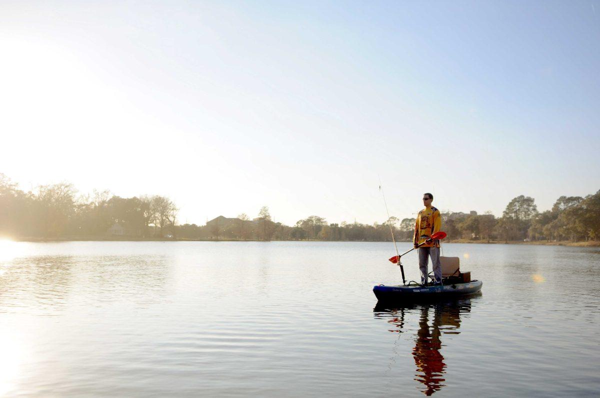 LSU Kayak Fishing Club member, Jacob Cormier, stands on his kayak holding his paddle on the Milford Wampold Memorial Park Lake.