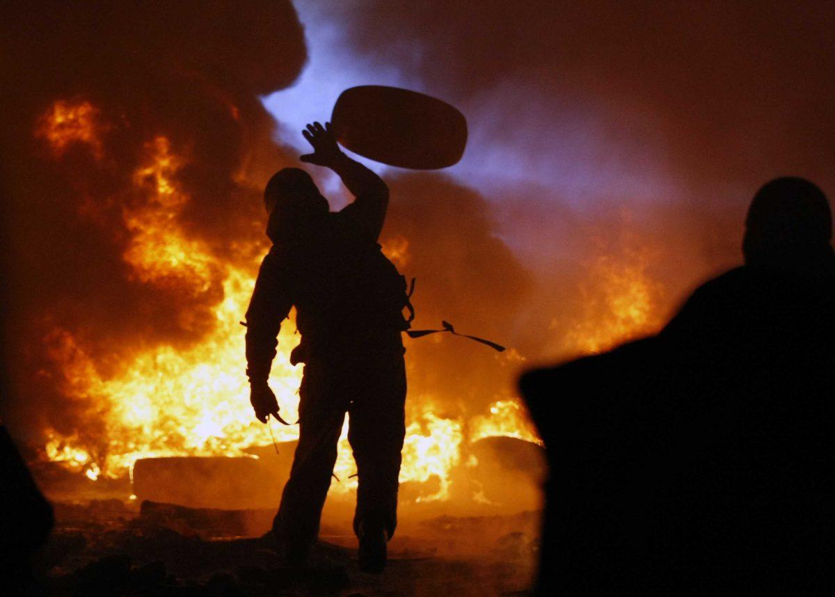 A protester throws a tire onto a fire during clashes with police in central Kiev, Ukraine, Friday Jan. 24, 2014. As riots spread from Ukraine's embattled capital to nearly half of the country, President Viktor Yanukovych promised Friday to reshuffle his government and make other concessions &#8212; but a top opposition leader said nothing short of his resignation would do. Hours after the president's comments, huge fireballs lit up the night sky in central Kiev and plumes of thick black smoke rose from burning tires at giant barricades erected by protesters. (AP Photo/Darko Vojinovic)