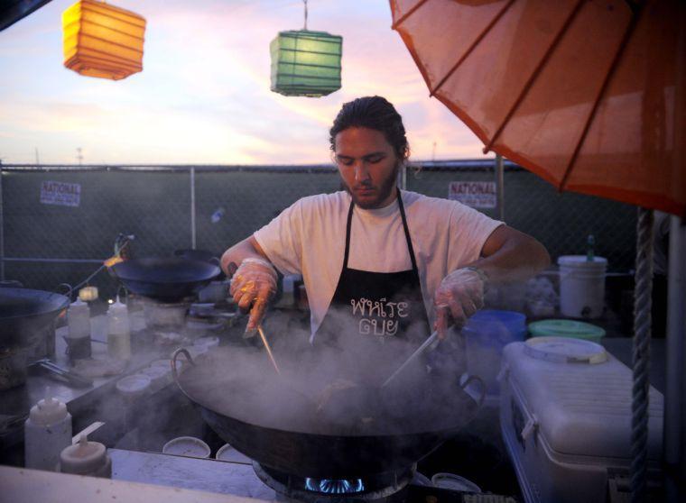 White Guy Pad Thai cook stirs rice noodles in a wok at the food vending area of Buku Music + Art Project at Mardi Gras World in New Orleans.