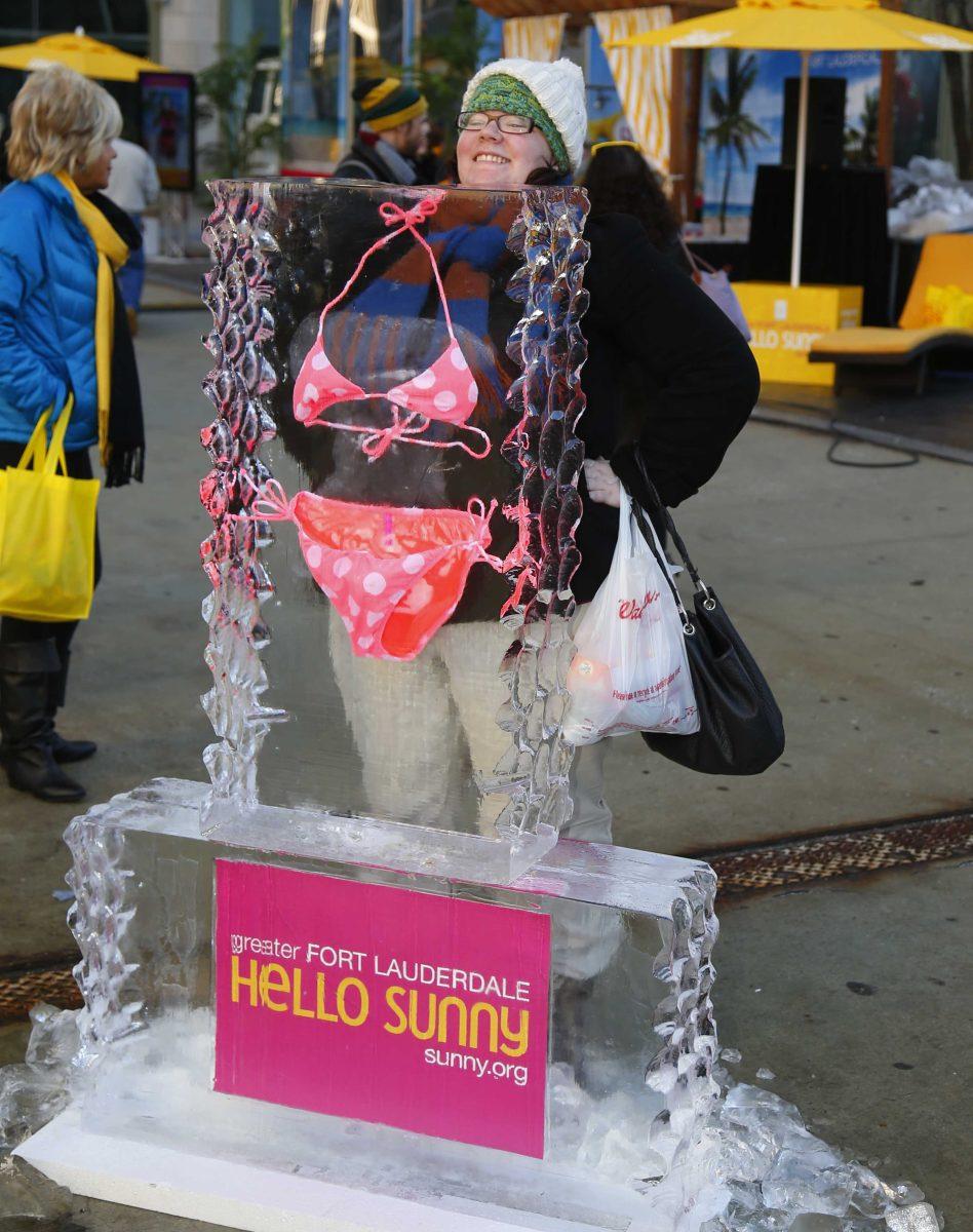 IMAGE DISTRIBUTED FOR GREATER FORT LAUDERDALE - A woman poses in front of an ice sculpture with a swim suit frozen inside of it during the Hello Sunny beach promotion, hosted by the Greater Fort Lauderdale Convention &amp; Visitors Bureau in Tribune Plaza, on Wednesday, Feb. 19, 2014, in Chicago. Visit sunny.org for more information. (Photo by Jeff Haynes/Invision for Greater Fort Lauderdale/AP Images)