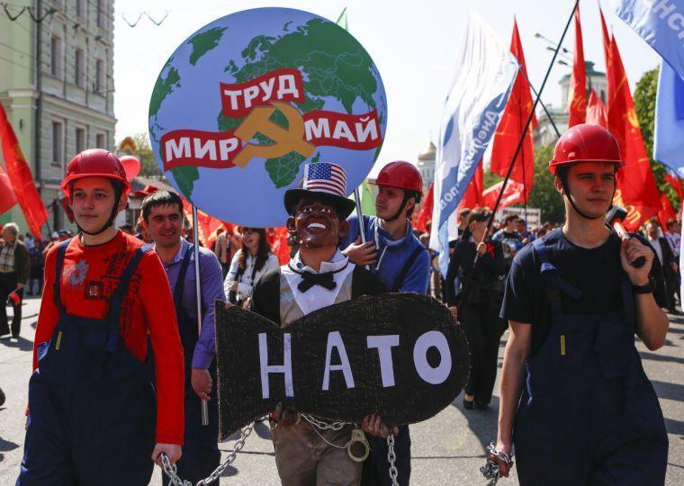 People in helmets (left and right), dressed as Russian factories workers, hold a man wearing Barack Obama's mask with mock NATO's bomb in chains, as they take part in a Communists demonstration in downtown Moscow, Russia, Thursday, May, 1, 2014. Thousands of Communists, members of Russia's main political parties and opposition activists staged competing marches in Moscow and other cities Thursday marking the traditional May Day holiday. Poster at the background reads : Peace, Labour, May. (AP Photo/Denis Tyrin)