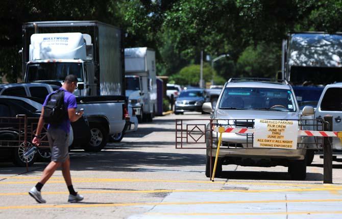 A student walks past cars and trucks gathered for the filming of a movie on campus Wednesday, June 18, 2014 near the student union.