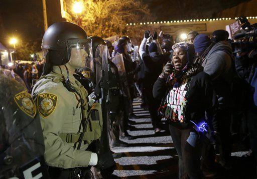 Police officers stand guard as protesters react to the announcement of the grand jury decision not to indict police officer Darren Wilson in the fatal shooting of Michael Brown, an unarmed black 18-year-old, Monday, Nov. 24, 2014, in Ferguson, Mo. (AP Photo/David Goldman)