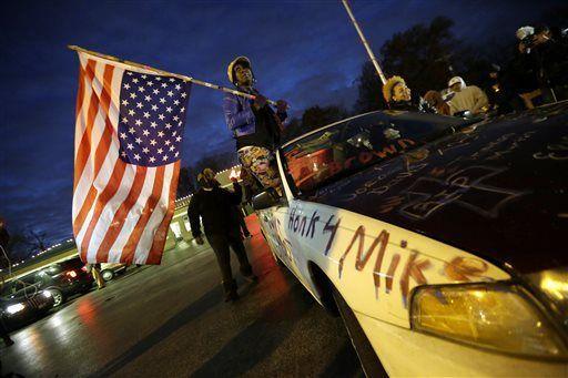 Gina Gowdy holds an upside-down American flag Monday, Nov. 24, 2014, in Ferguson, Mo., more than three months after an unarmed black 18-year-old man was shot and killed there by a white policeman. Ferguson and the St. Louis region are on edge in anticipation of the announcement by a grand jury whether to criminally charge Officer Darren Wilson in the killing of 18-year-old Michael Brown. (AP Photo/Charlie Riedel)