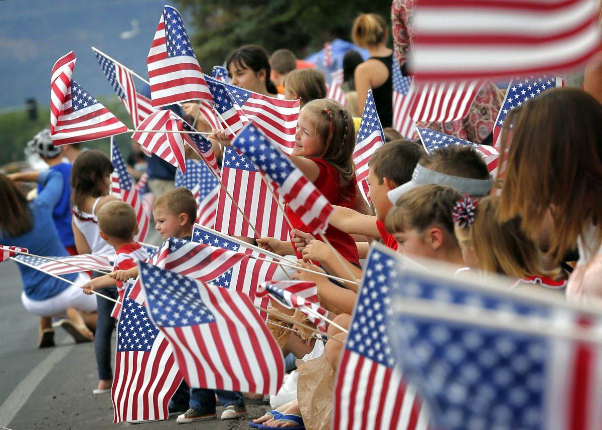 People wave flags as the Independence Day parade rolls down Main Street, Friday, July 4, 2014, in Eagar, Ariz. The Northern Arizona town celebrates the Fourth of July annually with a parade and fireworks. (AP Photo/Matt York)