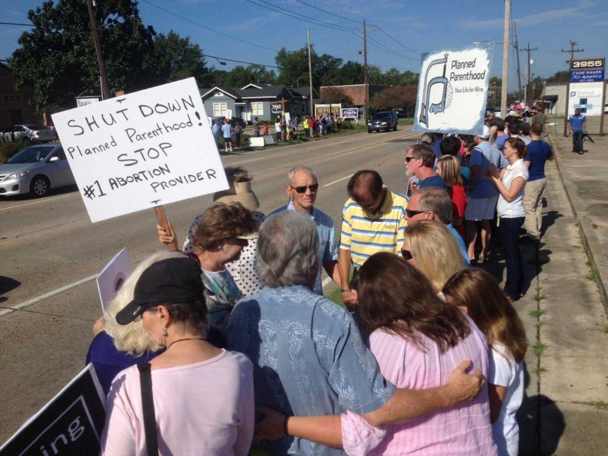 Protesters brandish signs and pray together Saturday morning outside the Planned Parenthood building on Government Street.