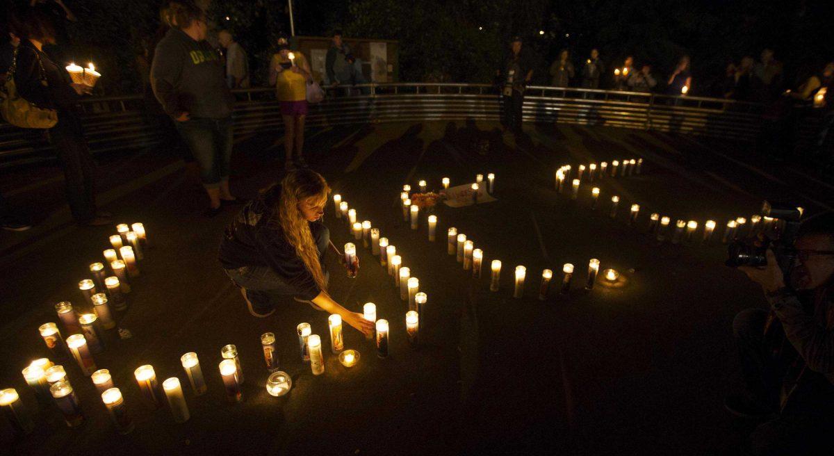 Amanda Calvert, a former student at Umpqua Community College, helps to spell the initials of the school with candles during a vigil at Stewart Park in Roseburg, Ore., after a fatal shooting at the school Thursday, Oct. 1, 2015. (Chris Pietsch/The Register-Guard via AP) MANDATORY CREDIT