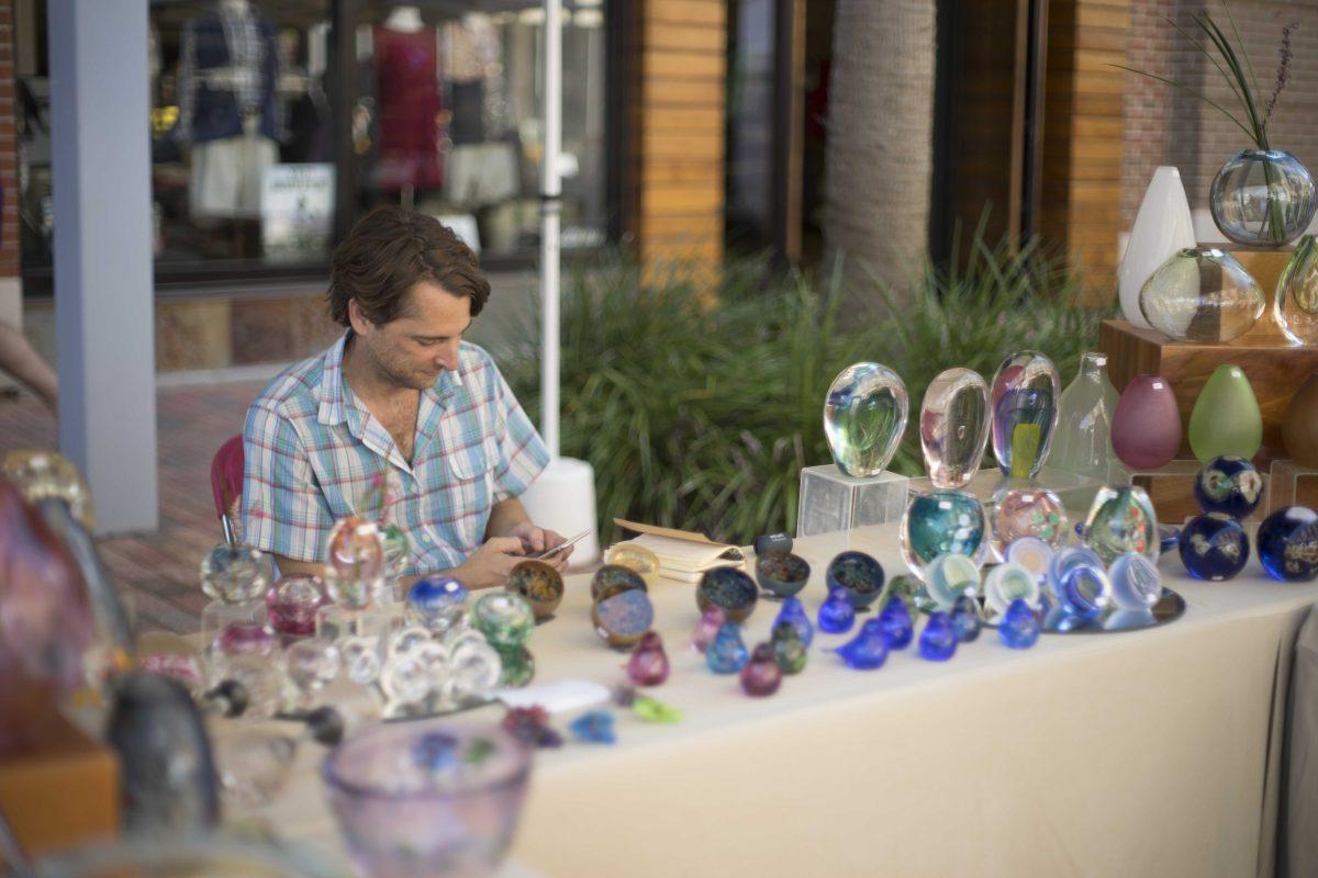 Glassblower Jeremy Ballard sits with a selection of his work on Sunday Sept. 25, 2016, during the 7th Annual Perkins Rowe Art Festival.