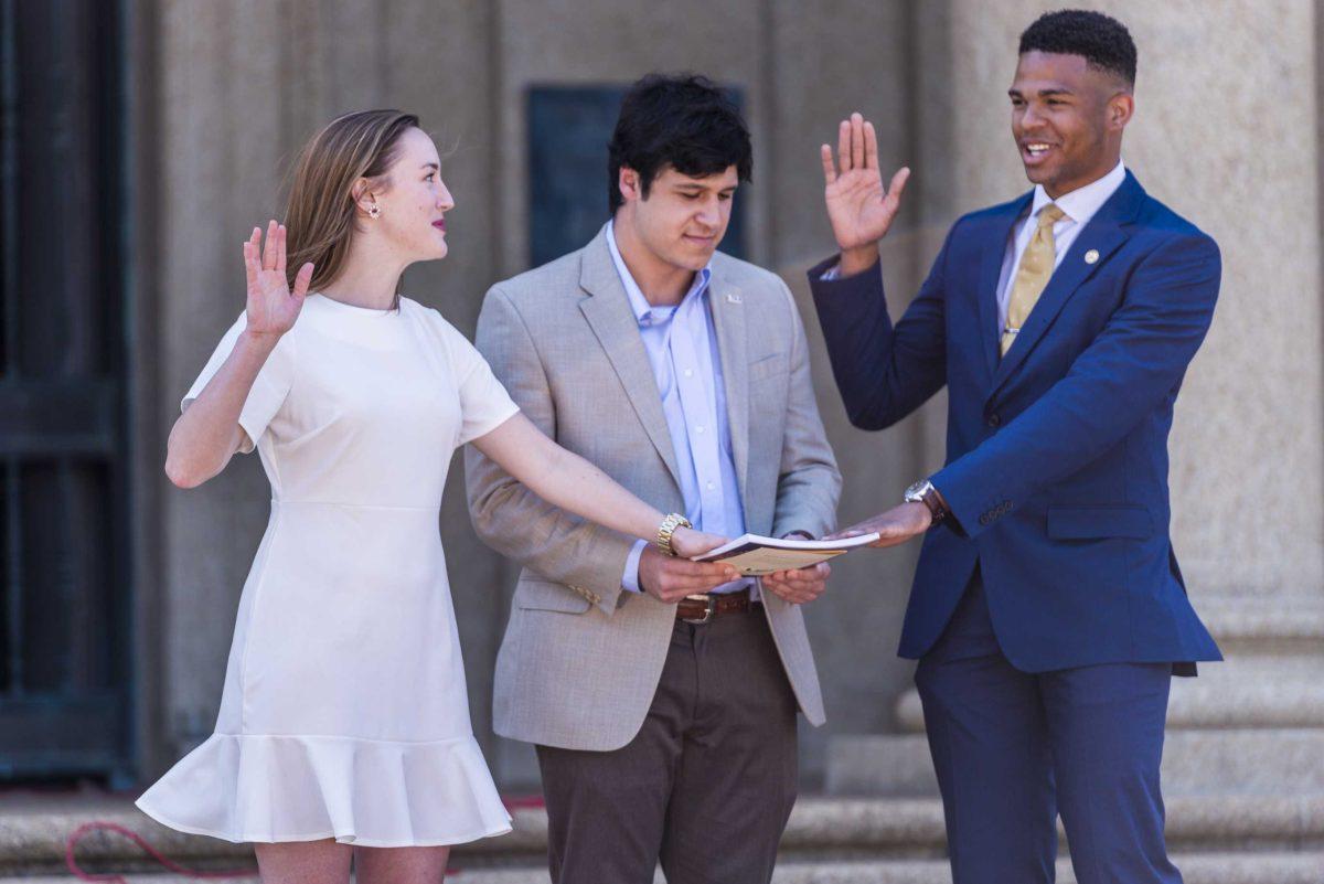 LSU Student Government president-elect Stewart Lockett (right) and vice president-elect Rachel Campbell (left) put their hands on the constitution, held by 2017-18 university court speaker James Mickler (center), as they are sworn into office during LSU's 2018-19 Student Government inauguration on Wednesday, April 4, 2018, near Memorial Tower.