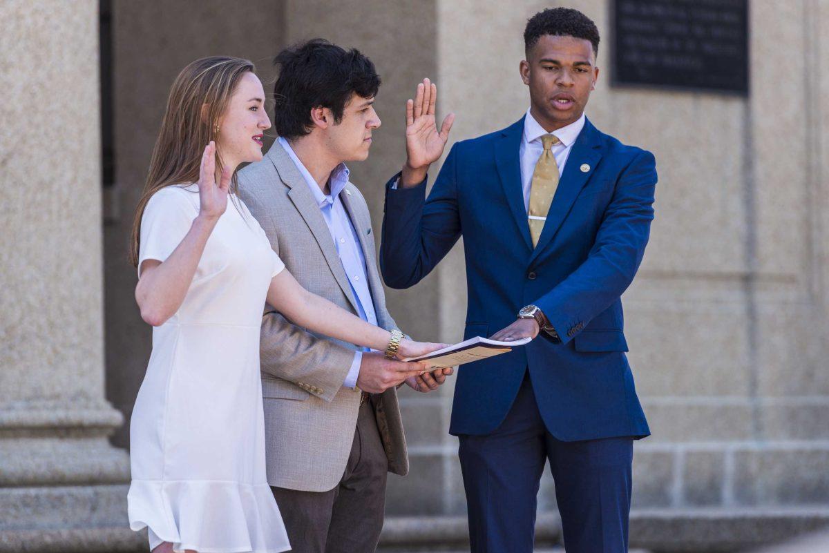 LSU Student Government president-elect Stewart Lockett (right) and vice president-elect Rachel Campbell (left) put their hands on the constitution, held by 2017-18 university court speaker James Mickler (center), as they are sworn into office during LSU's 2018-19 Student Government inauguration on Wednesday, April 4, 2018, near Memorial Tower.