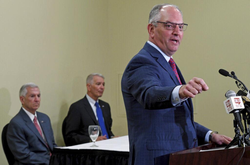 Louisiana Gov. John Bel Edwards speaks at the lectern as the Press Club of Baton Rouge hosts a forum for the three gubernatorial candidates Monday Sept. 23, 2019, in Baton Rouge, La. Gov. John Bel Edwards, a Democrat, faced his two Republican challengers, U.S. Rep. Ralph Abraham, , right at table background, who has represented Louisiana's fifth congressional district since 2015, and businessman Eddie Rispone, of Baton Rouge, left at table background. (Bill Feig/The Advocate via AP)