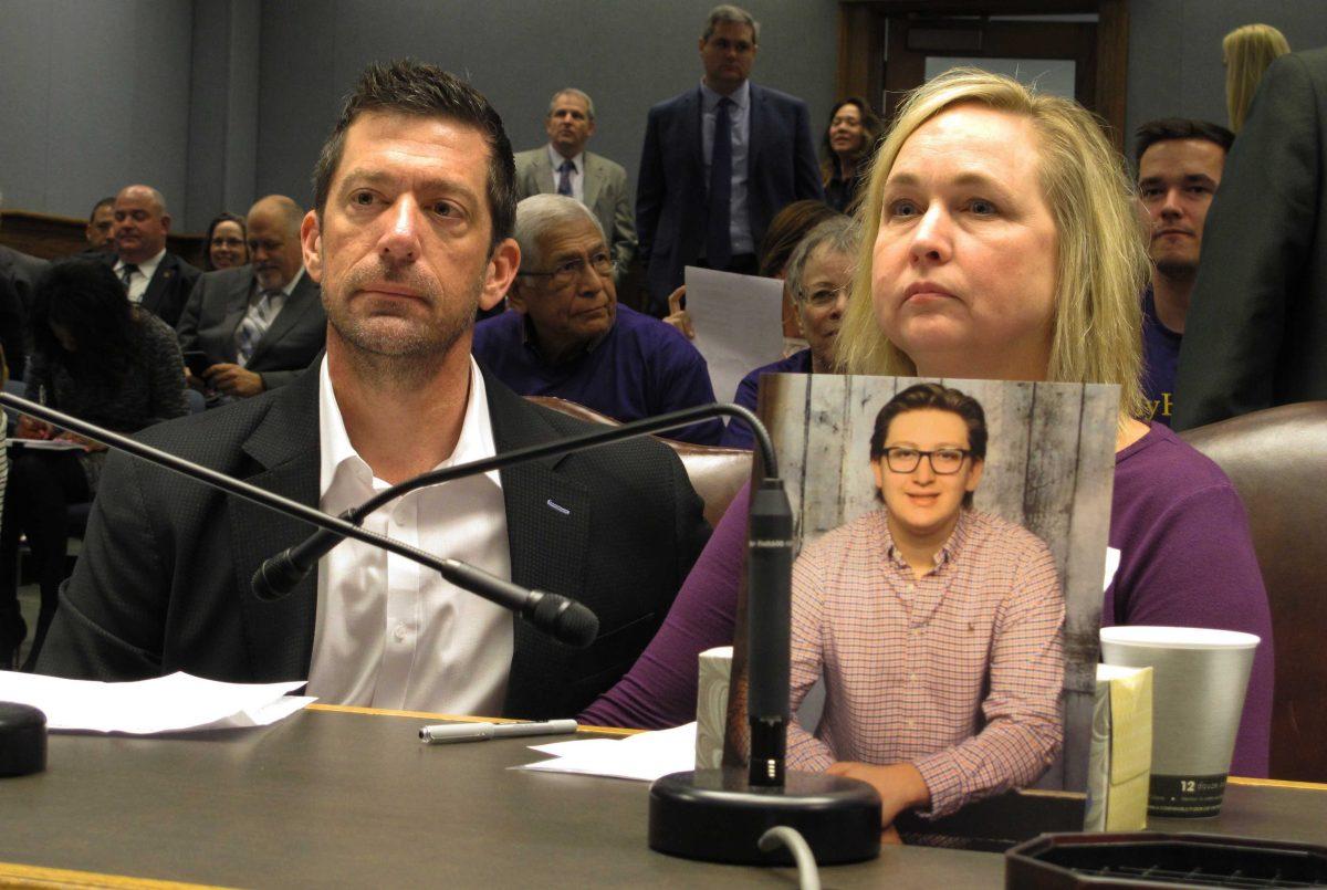 FILE - In this Wednesday, March 21, 2018, file photo, Stephen and Rae Ann Gruver sit in a House committee room behind a photo of their son, 18-year-old Maxwell Gruver, a Louisiana State University freshman who died with a blood-alcohol content six times higher than the legal limit for driving in what authorities say was a hazing incident, in Baton Rouge, La. A federal appeals court says Stephen and Rae Ann Gruver can pursue a lawsuit that says the university disciplines sororities and fraternities differently because of gender. (AP Photo/Melinda Deslatte, File)