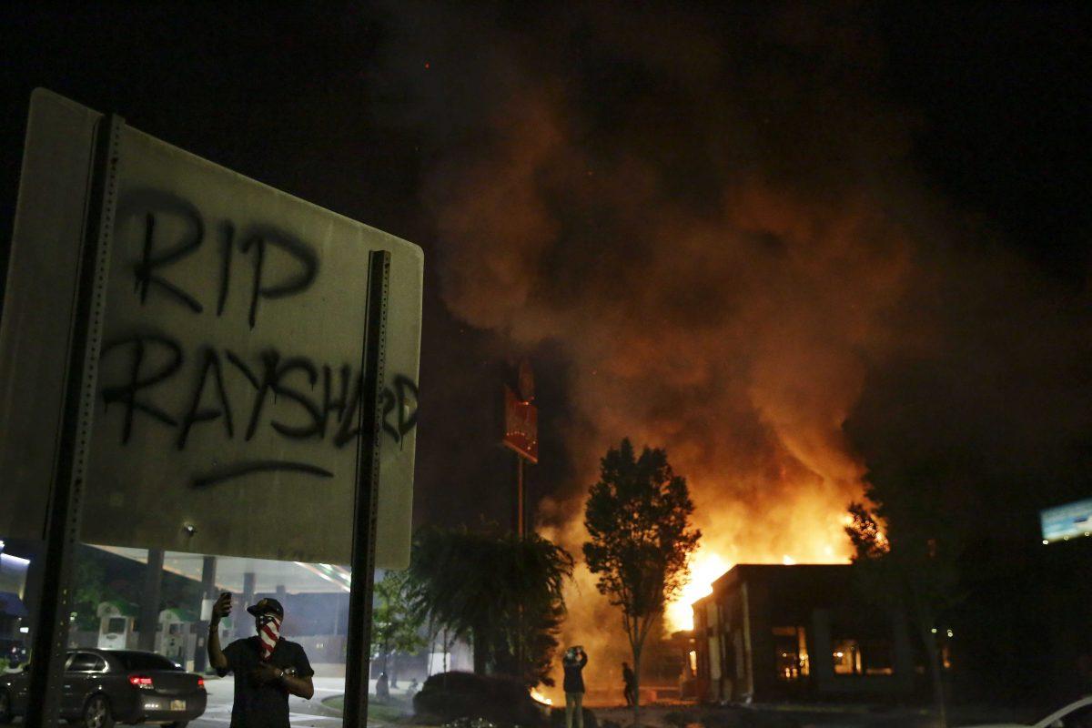 "RIP Rayshard" is spray painted on a sign as as flames engulf a Wendy's restaurant during protests Saturday, June 13, 2020, in Atlanta. The restaurant was where Rayshard Brooks was shot and killed by police Friday evening following a struggle in the restaurant's drive-thru line. (AP Photo/Brynn Anderson)