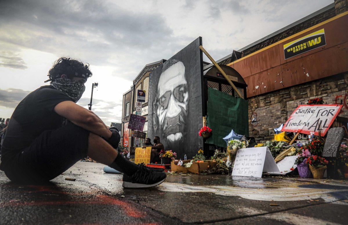 After a new mural, center, of George Floyd is added to a growing memorial of tributes, Trevor Rodriquez sits alone at the spot where Floyd died while in police custody, Tuesday June 2, 2020, in Minneapolis, Minn. "I have been out every single night protesting peacefully, just trying to support everything," said Rodriquez. "I didn't want to come here just on a rush, so I had to just take a moment to pay my respect." (AP Photo/Bebeto Matthews)