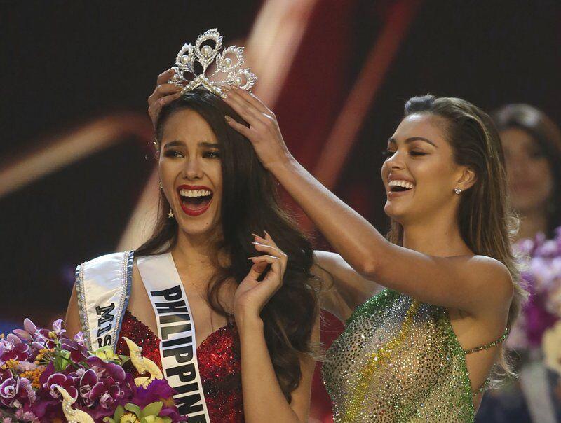 FILE - Catriona Gray of the Philippines, left, reacts as she is crowned the new Miss Universe 2018 by Miss Universe 2017 Demi-Leigh Nel-Peters during the final round of the 67th Miss Universe competition in Bangkok, Thailand, on Dec. 17, 2018. After a year and a half, the Miss Universe competition will return with a live telecast on May 16. The 69th Miss Universe will be crowned at the Seminole Hard Rock Hotel &amp; Casino Hollywood. (AP Photo/Gemunu Amarasinghe, File)