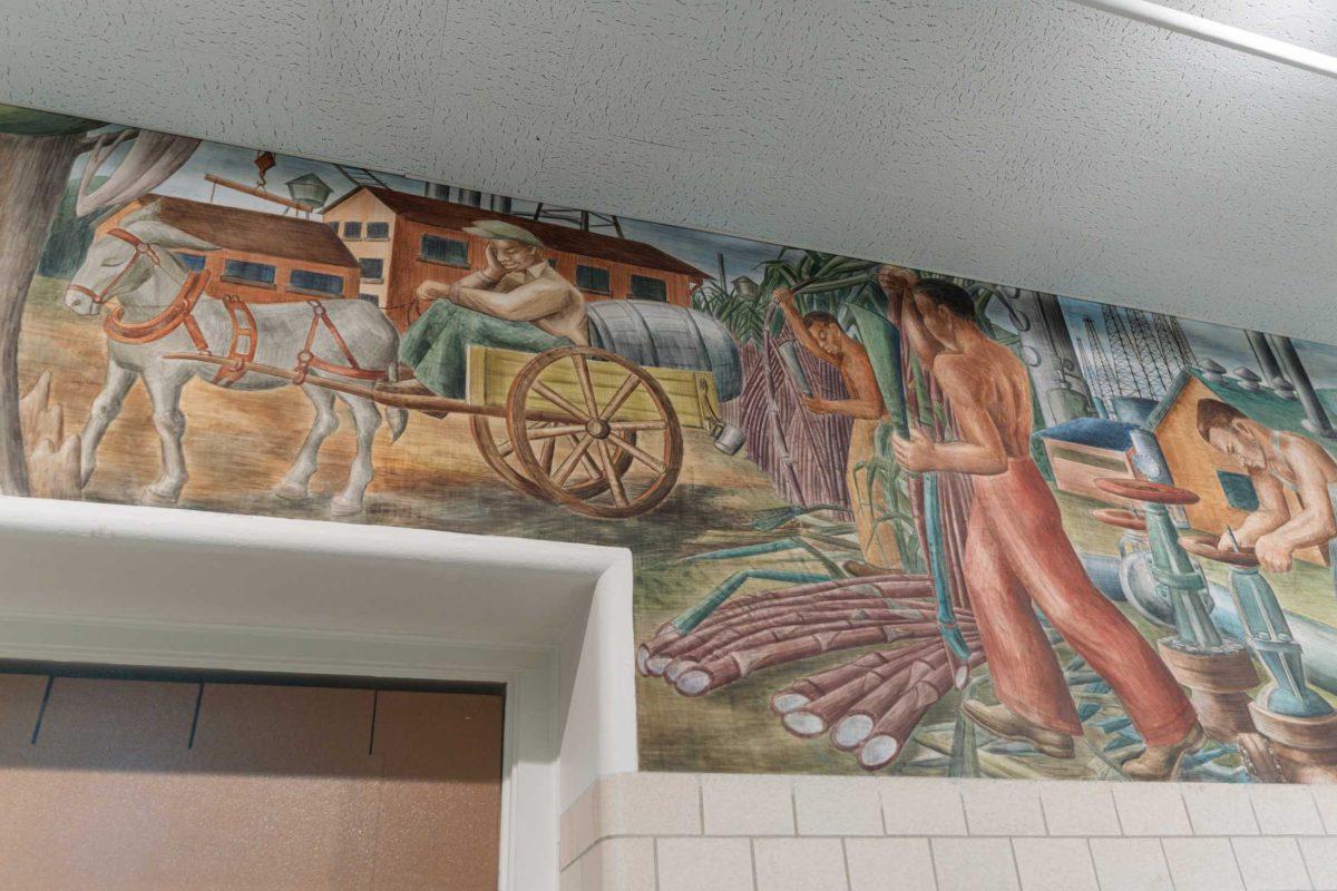 A painting of workers laboring in the sugarcane fields sits alongside a painting of a man sleeping in a wagon as seen in an April 14, 2021 image from within Allen Hall on LSU&#8217;s campus.