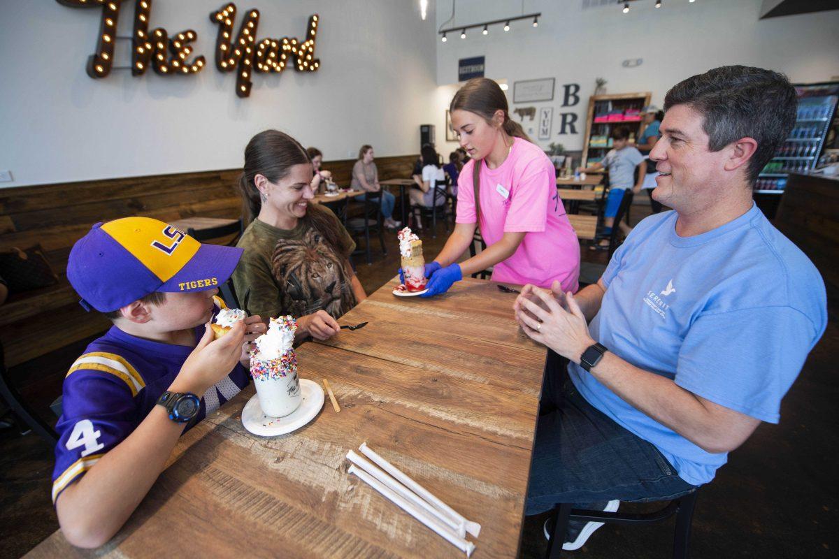 From left, Xander Hall, 9, of Prairieville, La., and his mother Nikki Hall, get served by Angelina Trancina, 17, with Xander's father John Hall at The Yard Milkshake Bar, Tuesday, July 13, 2021 in Baton Rouge, La. To say The Yard Milkshake Bar serves over-the-top confections is a bit of an understatement. This is the description for its Tiger Deaux milkshake unique to Baton Rouge: a concoction of cookie dough ice cream with purple and gold marshmallow cream served in a vanilla iced jar rolled in purple and gold sprinkles and topped with purple and gold whipped cream, a scoop of chocolate chip cookie dough, more sprinkles and a purple tiger paw.(Travis Spradling/The Advocate via AP)