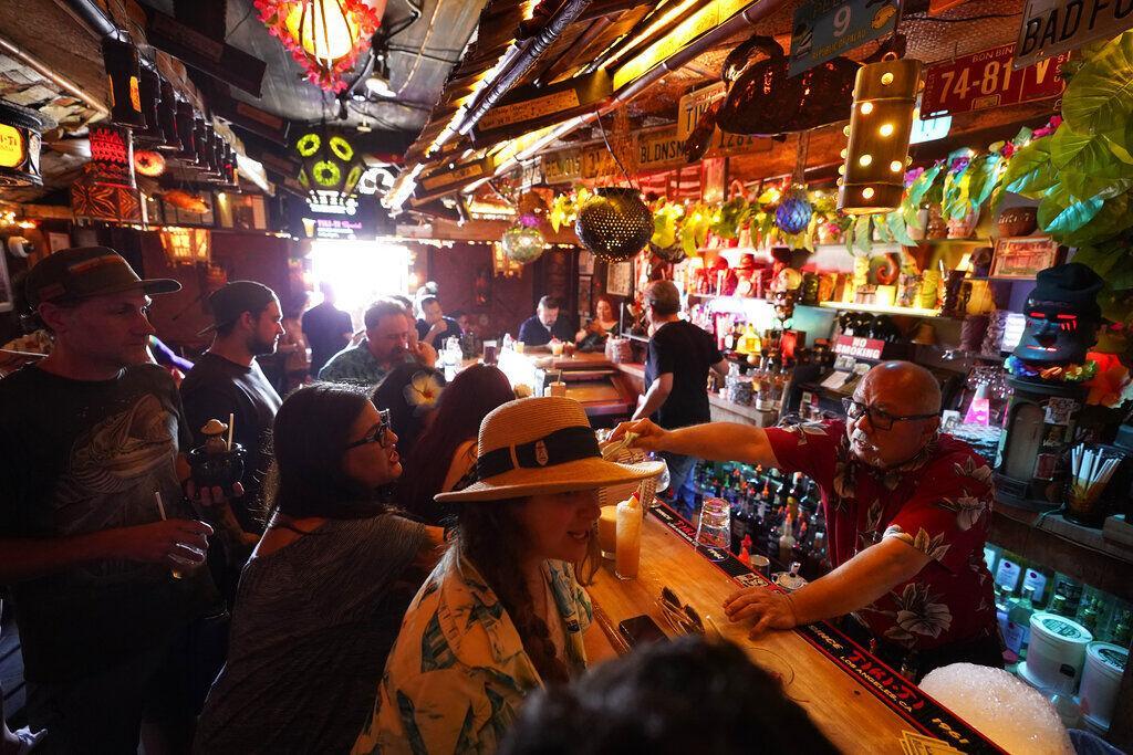 FILE - In this Wednesday, July 7, 2021, file photo, patrons enjoy cold tropical cocktails in the tiny interior of the Tiki-Ti bar as it reopens on Sunset Boulevard in Los Angeles. COVID-19 cases have doubled over the past three weeks, driven by the fast-spreading delta variant, lagging vaccination rates in some states and Fourth of July gatherings. Los Angeles County public health officials have urged people to resume wearing masks indoors regardless of their vaccination status. (AP Photo/Damian Dovarganes, File)