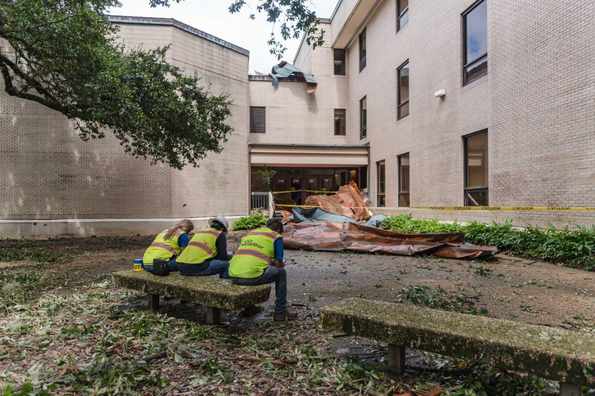 Three workers sit Monday, Aug. 30, 2021, near the fallen pieces of roofing the day after Hurricane Ida hit at the LSU School of Music on Infirmary Road.